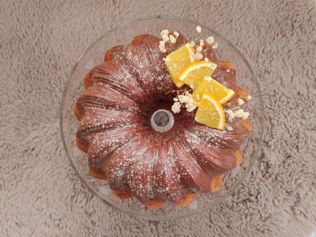 Un délicieux gâteau Bundt surmonté de tranches d'orange et de sucre en poudre sur une surface texturée.