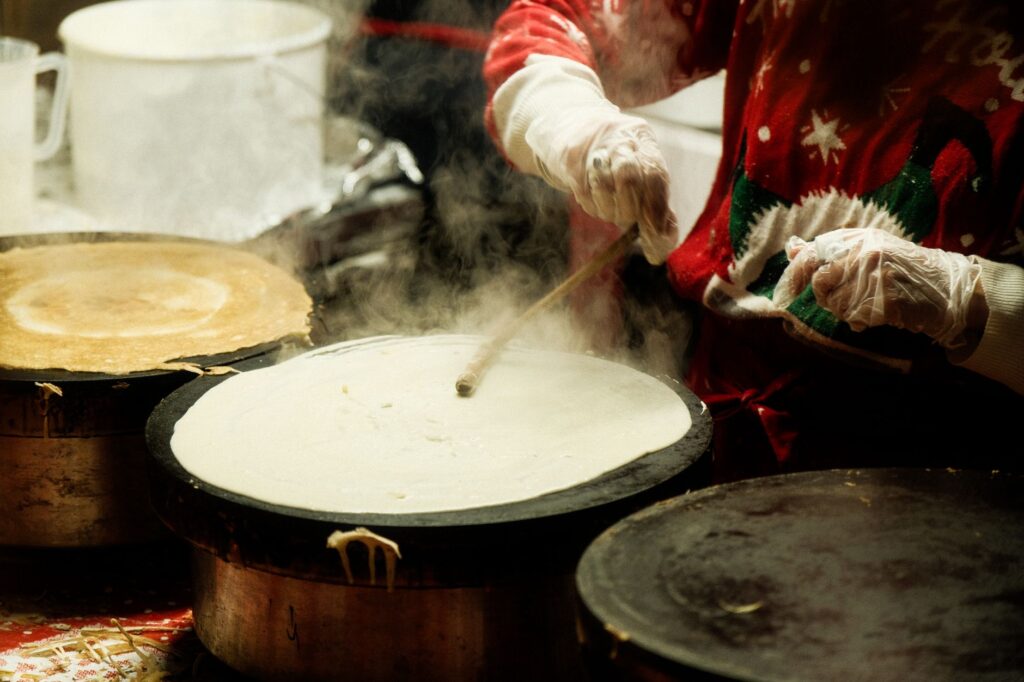 Personne fabriquant des crêpes à un stand de marché de Noël, portant un pull festif.