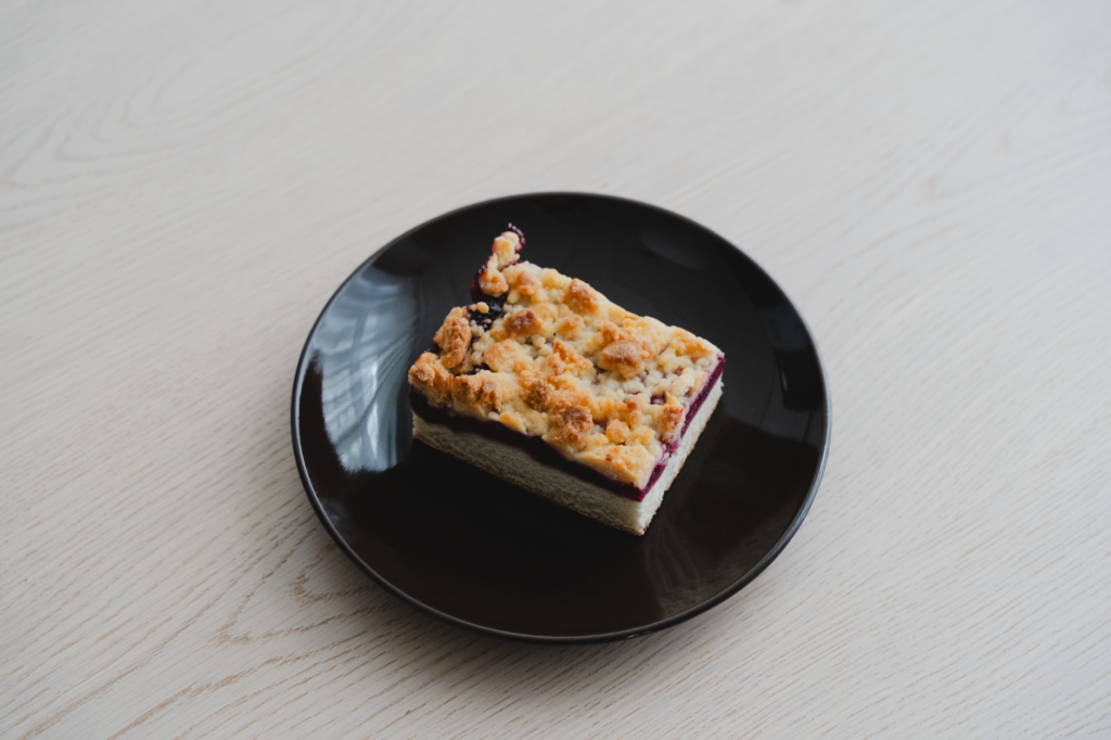 Une part alléchante de streuselkuchen fourrée aux fruits rouges, présentée sur une assiette noire, parfaite pour les amateurs de desserts.