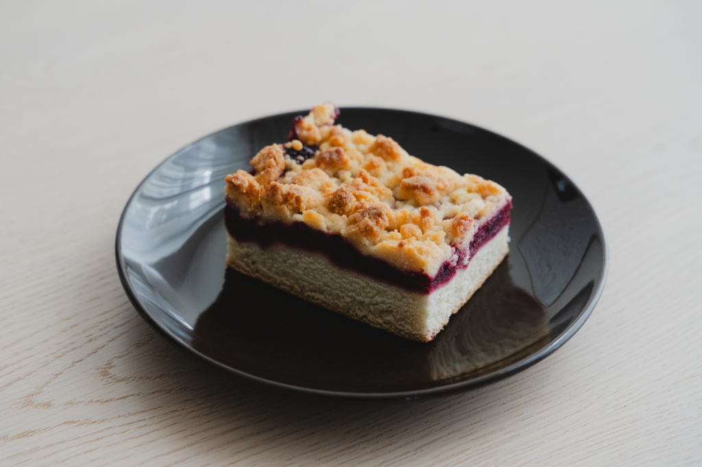 Une tranche délicieuse de Streuselkuchen aux baies avec un topping croustillant servie sur une assiette noire.