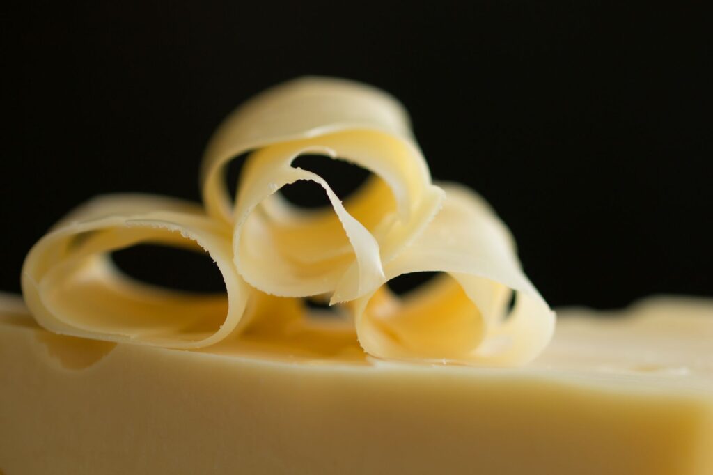 Gros plan de fines volutes de fromage sur fond sombre, mettant en valeur leur texture et leurs courbes.