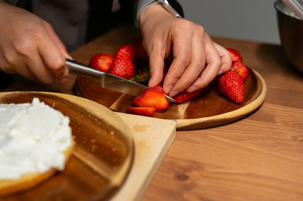 Gros plan sur des mains coupant des fraises fraîches pour décorer un gâteau.