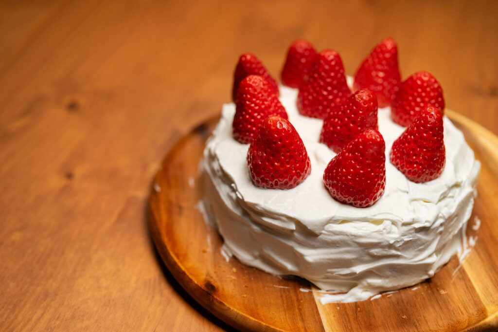 Un délicieux gâteau à la crème garni de fraises, présenté sur une assiette en bois, parfait pour les fêtes.