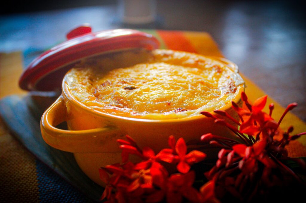 Plat chaud cuit au four dans un pot jaune, décoré de fleurs rouges éclatantes sur un linge coloré.
