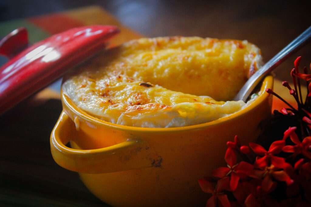 Plat salé recouvert de fromage fondu, servi dans un pot jaune à couvercle rouge.