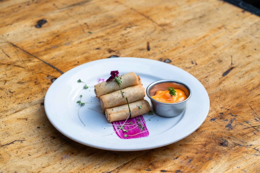 Rouleaux de printemps croustillants avec une sauce à tremper piquante sur une table en bois, garnis d'herbes.