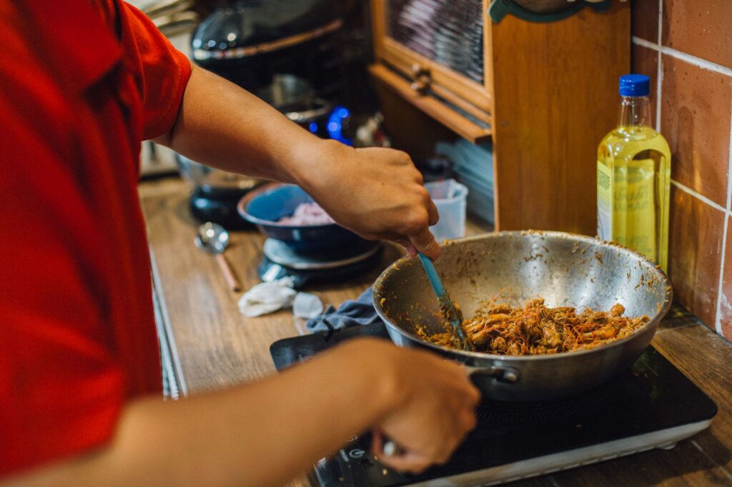 Personne cuisinant de la viande effilochée dans un wok sur une cuisinière, scène de cuisine à la maison.