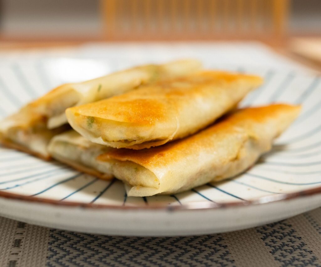 Des rouleaux de printemps dorés empilés sur une assiette en céramique rayée, parfaits pour les amateurs de cuisine asiatique.