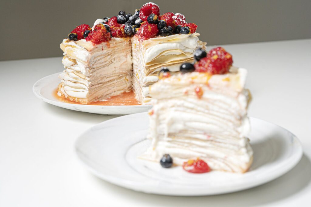 Un gâteau de crêpes à plusieurs étages garni de fruits rouges frais et de crème, parfait pour les amateurs de desserts.