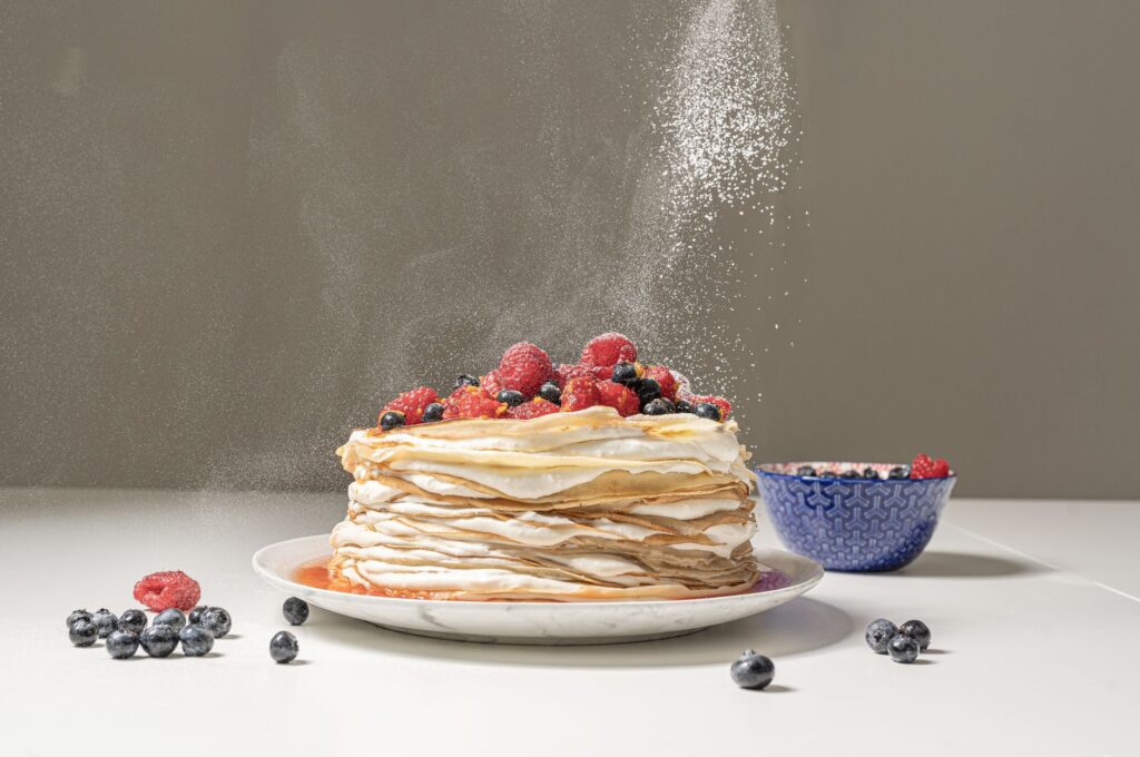 Délicieux gâteau de crêpes surmonté de baies fraîches et saupoudré de sucre, parfait pour les amateurs de dessert.