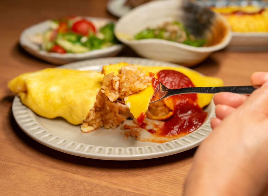 Gros plan sur un omurice japonais, un plat de riz à base d'omelette, servi avec du ketchup dans une assiette.