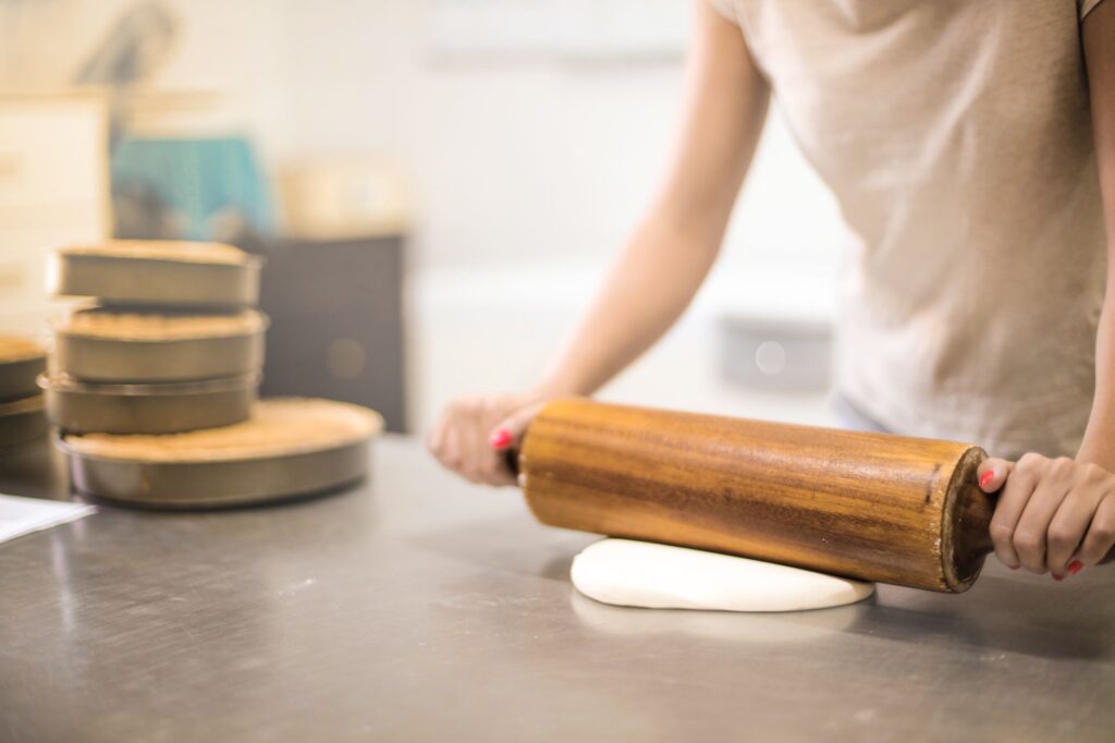 Une femme utilisant un rouleau à pâtisserie en bois pour aplatir la pâte dans une cuisine de boulangerie.