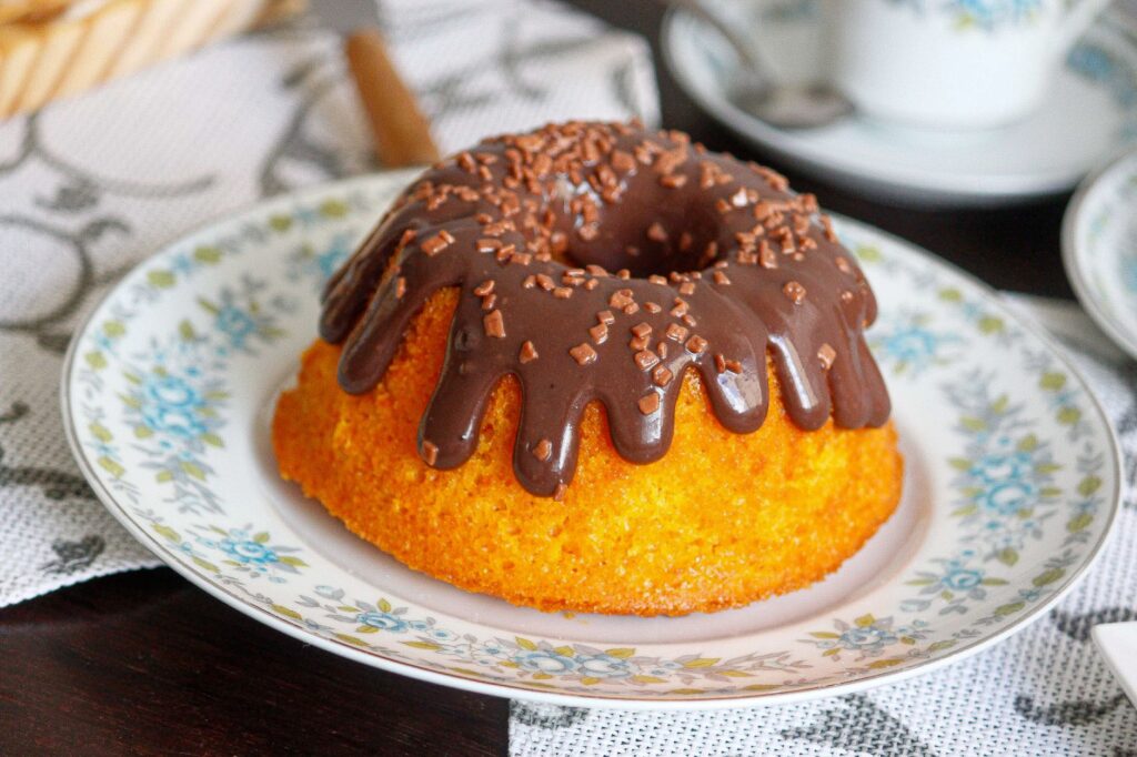 Gâteau aux carottes brésilien orné d'un riche filet de chocolat et de vermicelles, servi sur une assiette décorative.