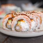 Gros plan alléchant de rouleaux de sushi au saumon et à l'avocat présentés sur une assiette en céramique magnifiquement travaillée.