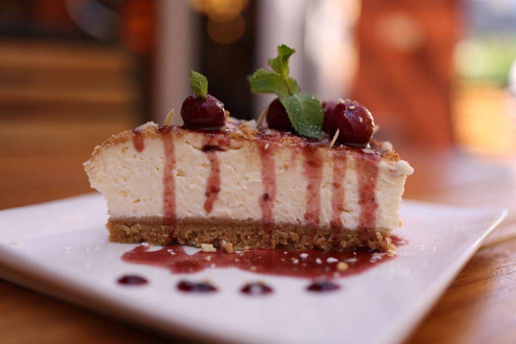 Gros plan sur une part de cheesecake crémeux garnie de cerises et de menthe.