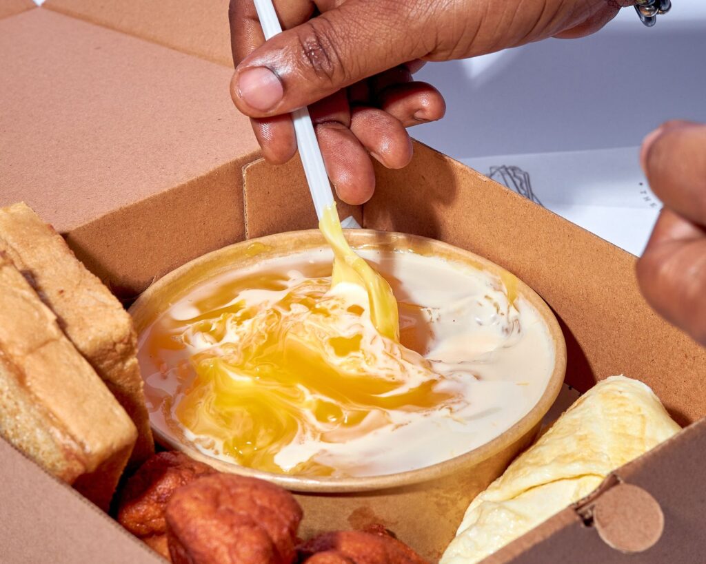 Gros plan sur une main mélangeant des sauces dans une boîte alimentaire avec des collations variées.