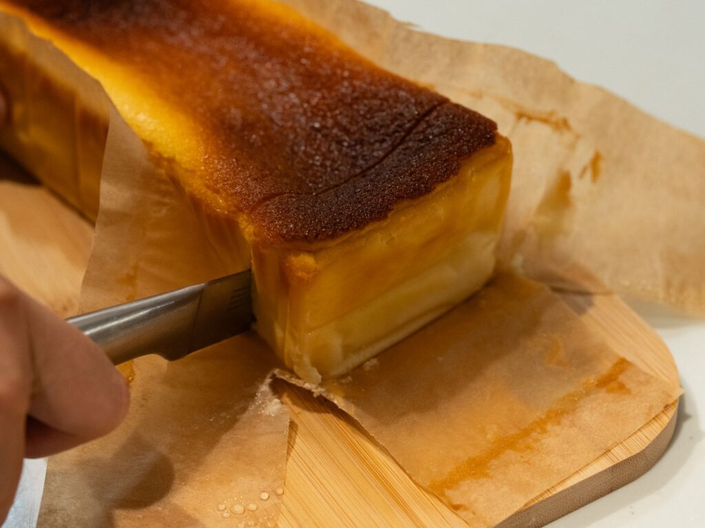 Une délicieuse part de cheesecake est coupée au couteau sur une planche en bois recouverte de papier sulfurisé.