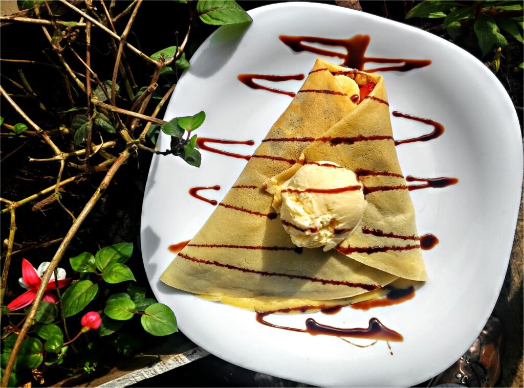 Une délicieuse crêpe française garnie de glace à la vanille et d'un filet de chocolat, dégustée en terrasse à Paris.