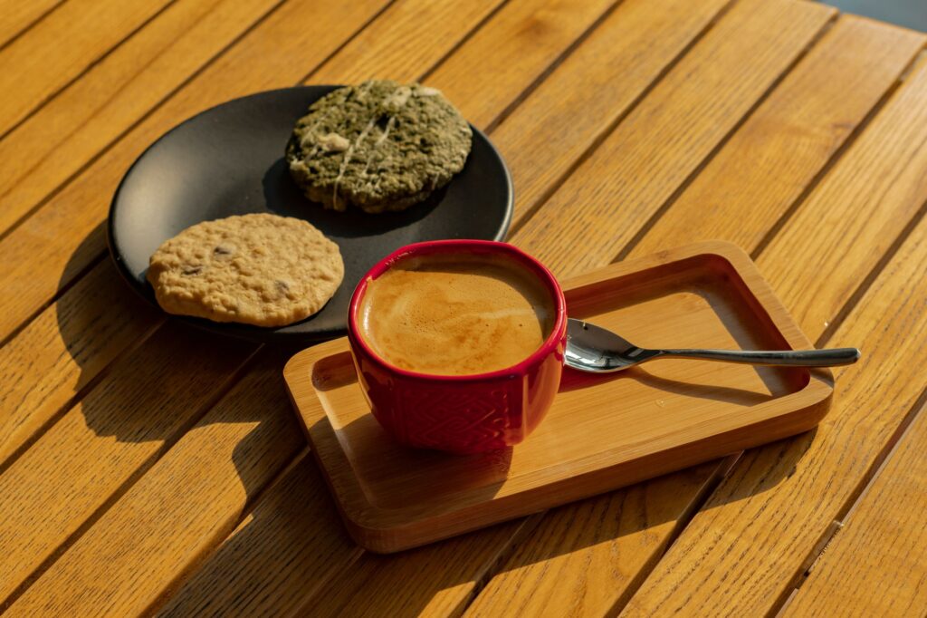 Une tasse de café chaud accompagnée de biscuits assortis, posée sur une table en bois baignée par la douce lumière du soleil.