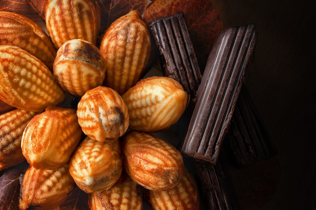 Gros plan de madeleines fraîchement cuites accompagnées de barres de chocolat riche sur un fond noir.