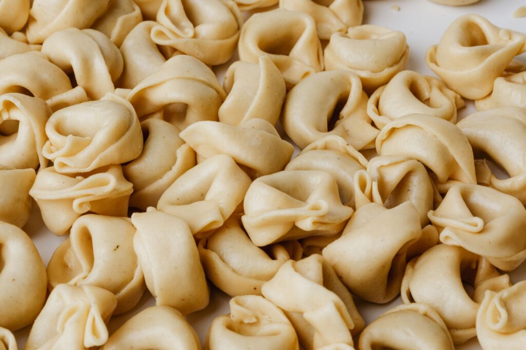 Vue en gros plan détaillée d'un tas de tortellinis maison crus, mettant en valeur la tradition culinaire italienne.