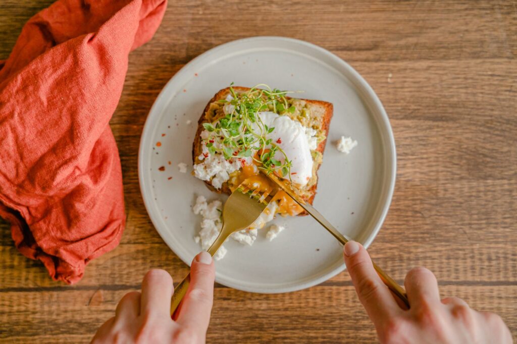 Gros plan sur un toast à l'avocat avec un œuf poché, servi avec une fourchette sur une table en bois.