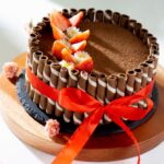 Délicieux gâteau au chocolat orné de fraises et d'un ruban rouge, parfait pour les célébrations.