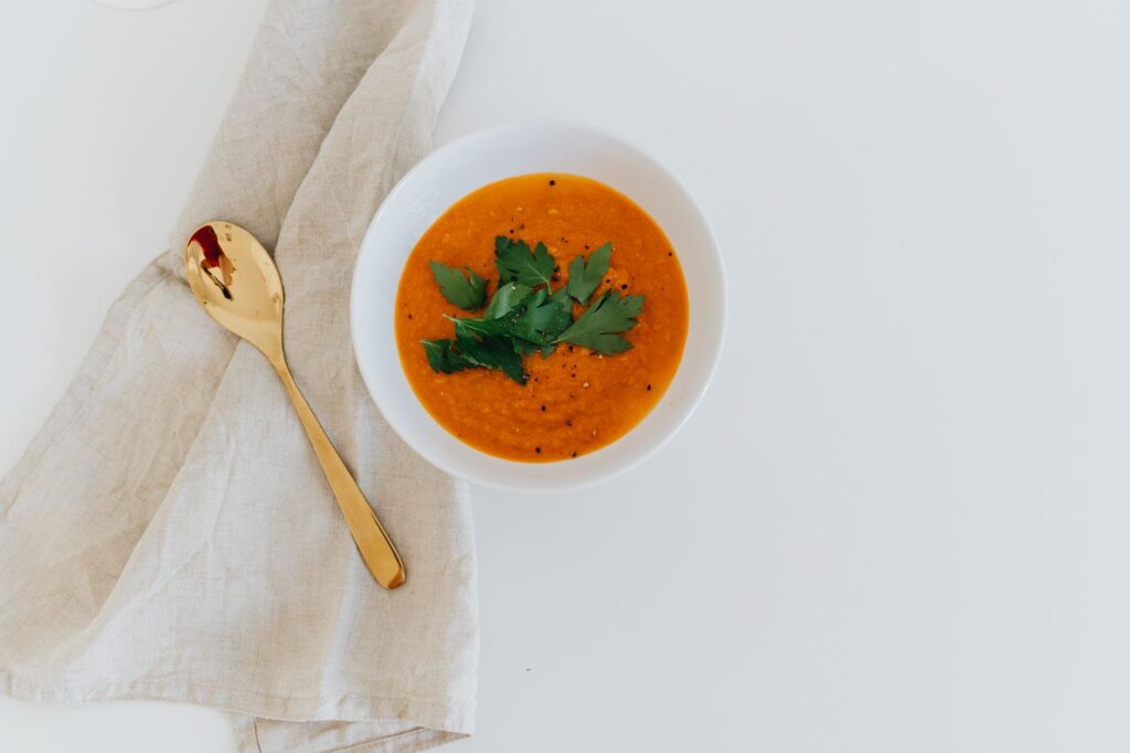 Bol élégant de soupe de carottes garni d'herbes fraîches sur fond blanc.