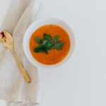 Bol élégant de soupe de carottes garni d'herbes fraîches sur fond blanc.