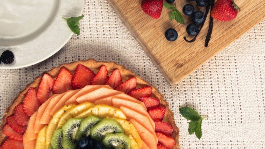 Vue de dessus d'une tarte aux fruits joliment présentée avec des fraises vibrantes, kiwi, et plus, sur un tapis tissé.