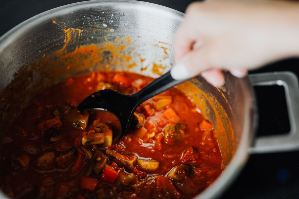Ragoût de légumes fraîchement cuisiné avec des tomates et des épices dans une casserole, mélangé à la main.