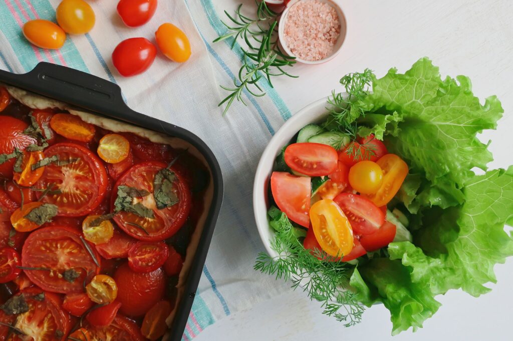 Vue de dessus d'une salade de légumes frais et d'un plat de tomates cuites sur une table claire.