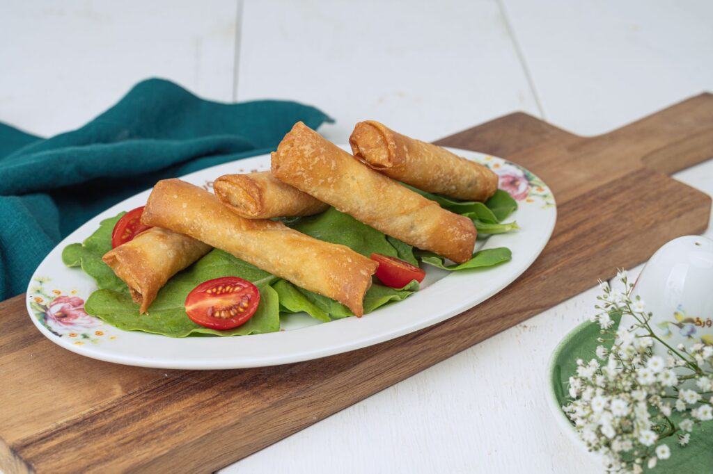 Rouleaux de printemps croustillants servis sur une assiette décorative avec de la laitue fraîche et des tomates cerises tranchées.