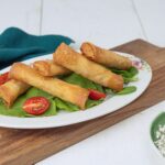 Rouleaux de printemps croustillants servis sur une assiette décorative avec de la laitue fraîche et des tomates cerises tranchées.