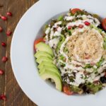 Vue de dessus d'une salade de quinoa fraîche avec avocat, tomate et sauce crémeuse sur une assiette.