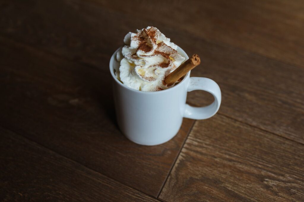 Un délicieux latte à la cannelle garni de crème fouettée servi dans une tasse blanche sur une table en bois.