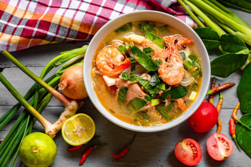 Délicieuse soupe thaïlandaise Tom Yum avec des crevettes, des herbes et des légumes frais, capturée en vue aérienne colorée.