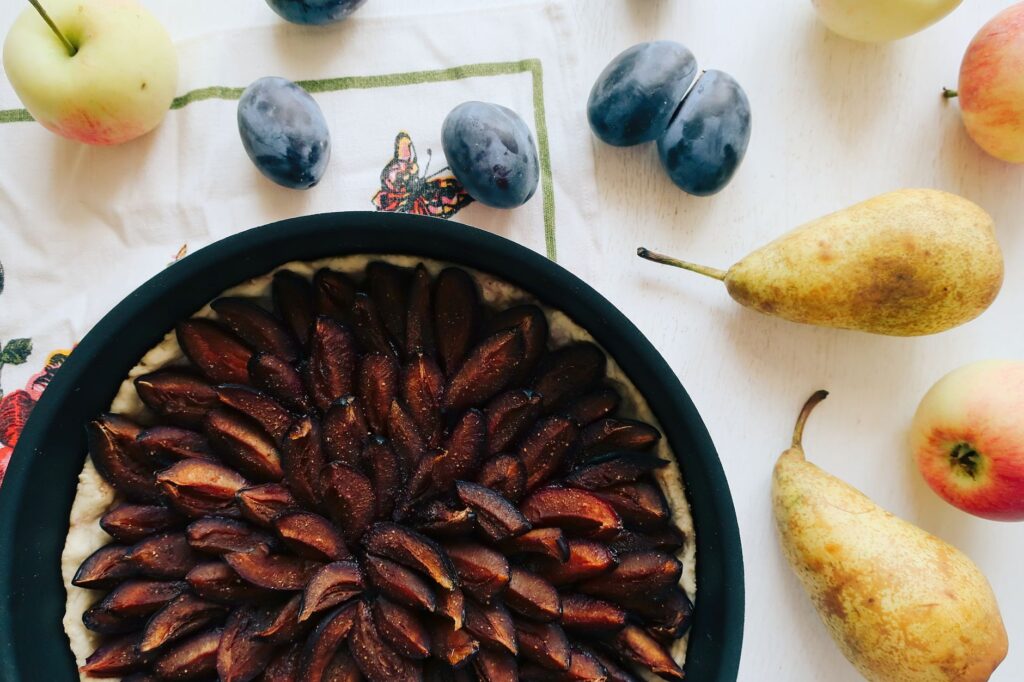 Un gros plan appétissant d'une tarte aux prunes entourée de pommes et de poires, parfait pour la photographie culinaire.