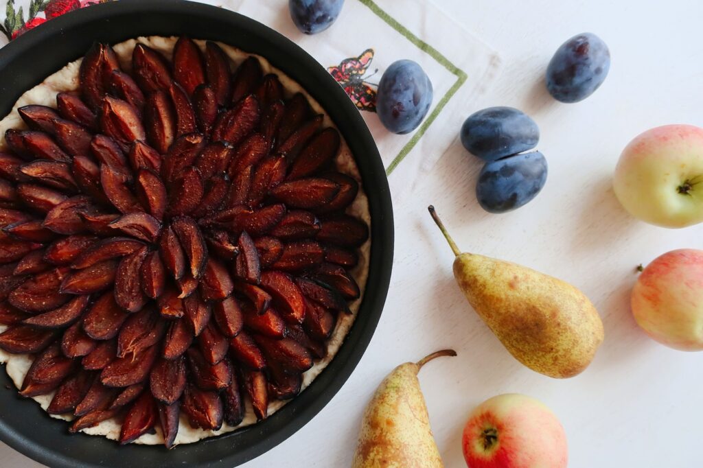 Une délicieuse tarte aux prunes entourée de fruits d'automne frais sur une table blanche.