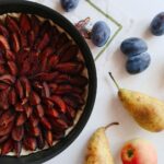 Une délicieuse tarte aux prunes entourée de fruits d'automne frais sur une table blanche.