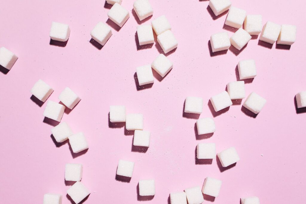 Plan rapproché de cubes de sucre dispersés sur une surface rose, moderne et lumineux.