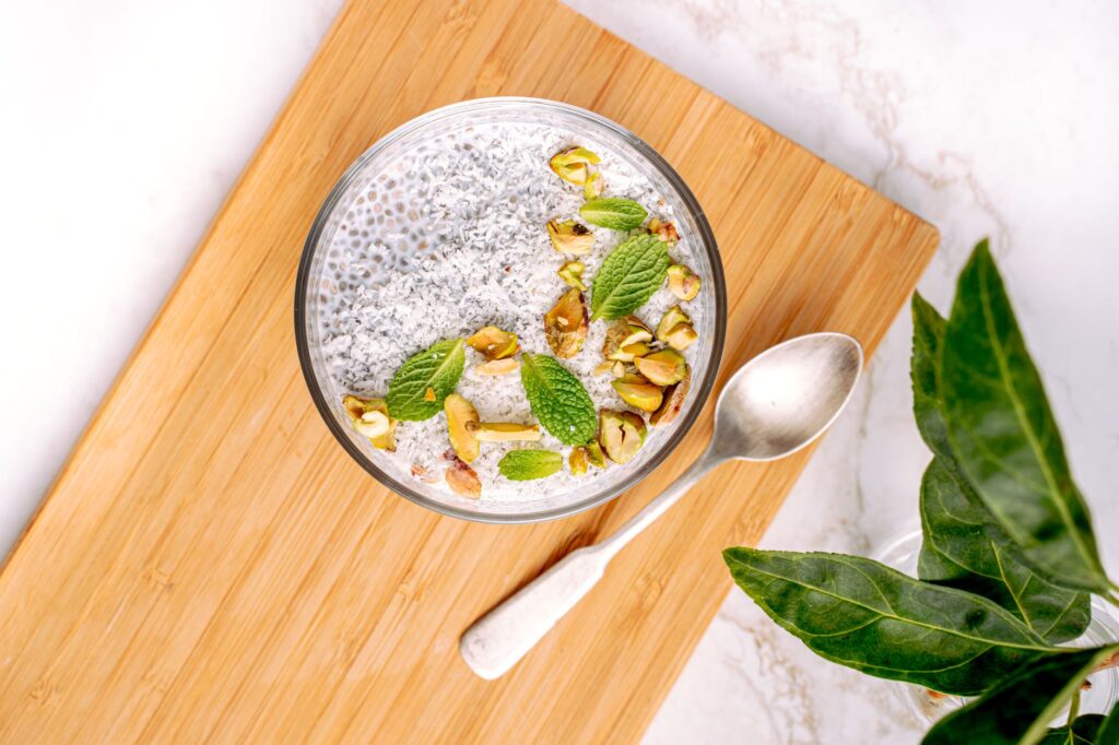 Vue de dessus d'un bol de pudding de graines de chia garni de pistaches et de feuilles de menthe sur une planche en bois.