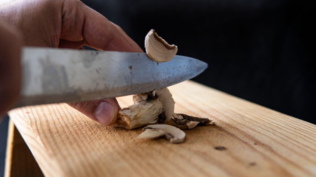 Gros plan sur une main tranchant des champignons sur une planche en bois dans une cuisine.