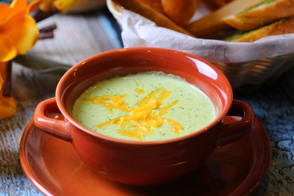 Gros plan sur une soupe crémeuse au brocoli dans un bol en terre cuite avec une garniture de cheddar.
