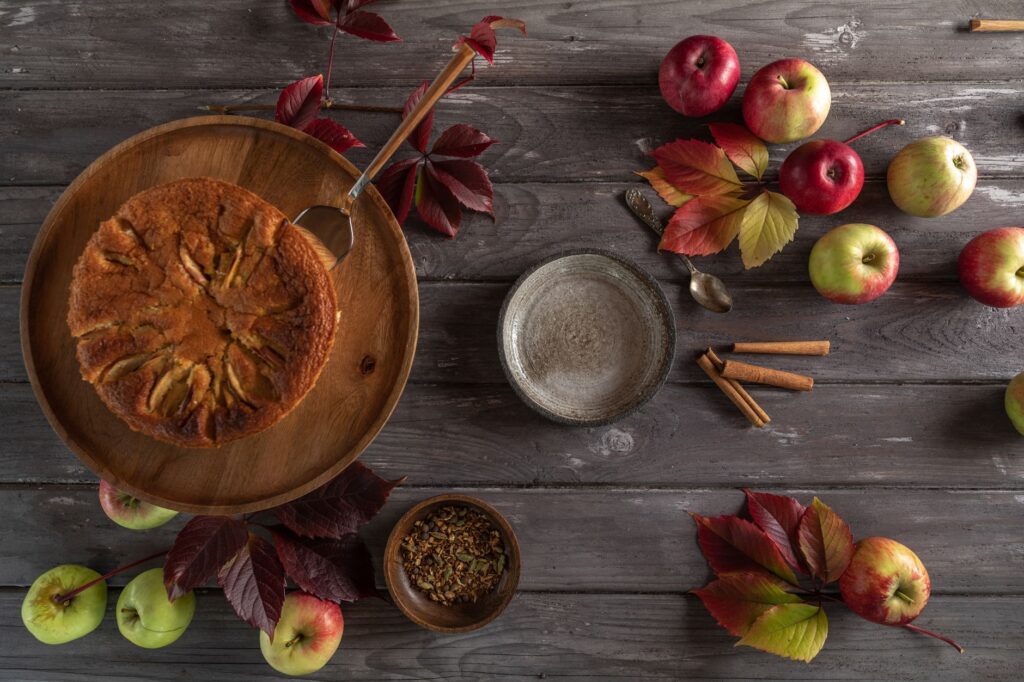 Vue du dessus d'une tarte aux pommes rustique entourée de pommes et de bâtons de cannelle sur une table en bois.