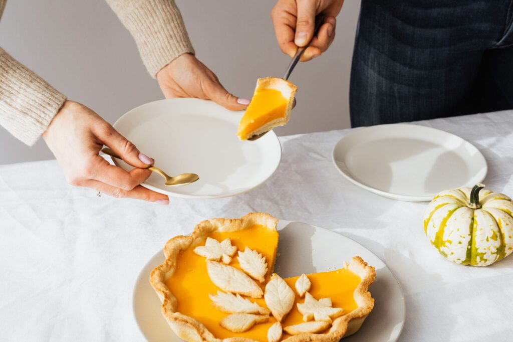 Une élégante part de tarte à la citrouille servie avec des assiettes blanches et une courge décorative sur une table.