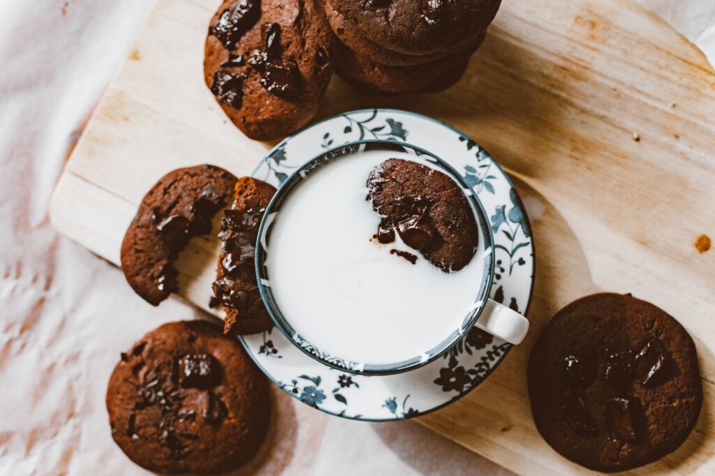 Vue de dessus de biscuits au chocolat faits maison avec une tasse de lait sur une surface en bois.