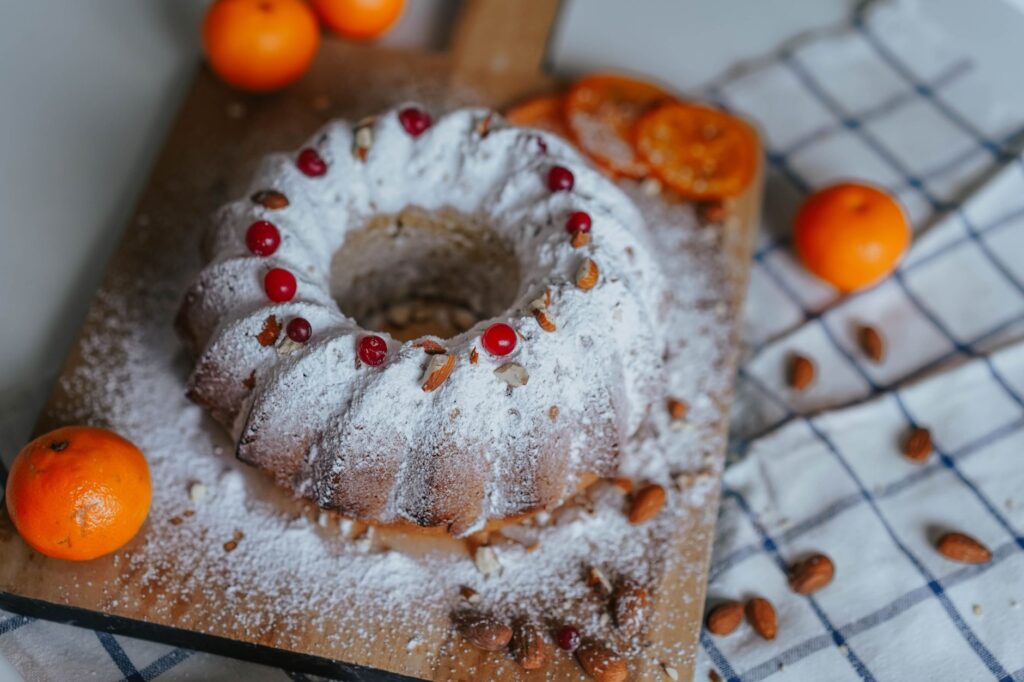 Un gâteau Bundt magnifiquement cuit, orné d'amandes et de tranches d'agrumes, délicatement saupoudré de sucre.