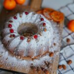 Un gâteau Bundt magnifiquement cuit, orné d'amandes et de tranches d'agrumes, délicatement saupoudré de sucre.