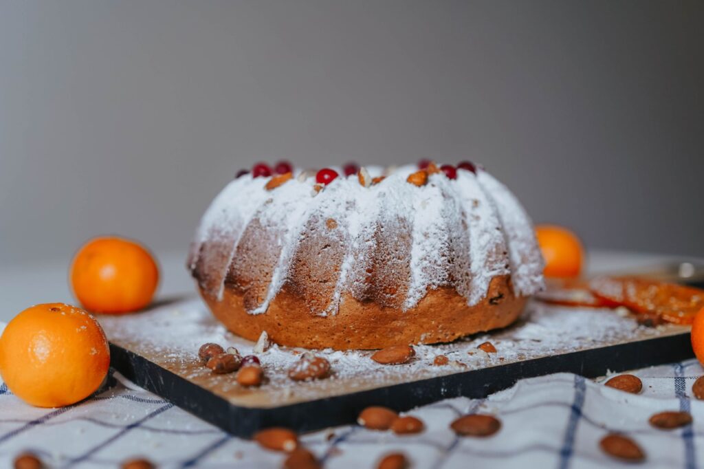 Gros plan d'un gâteau Bundt en poudre avec des oranges et des amandes sur un plateau.